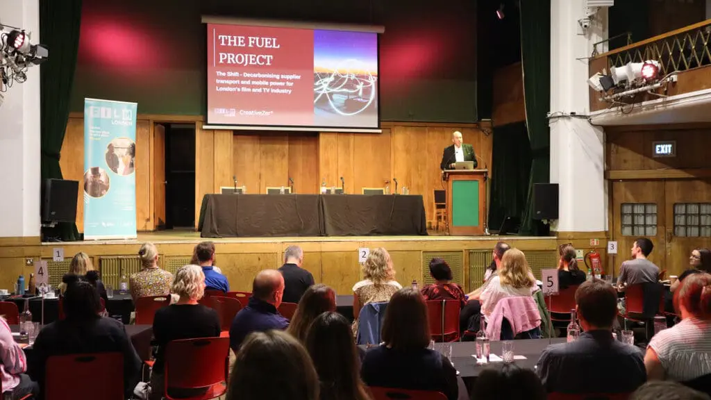 a conference with shot of audience looking at someone presenting on stage behind a lectern