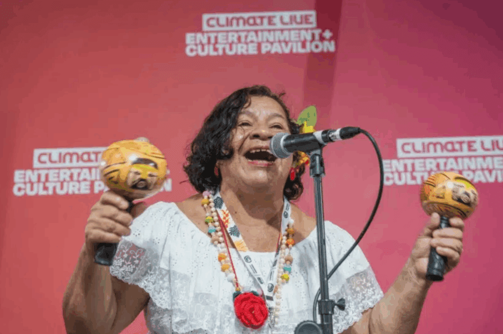 Claudete do Tijupa performs at COP singing into the microphone and shaking maracas.