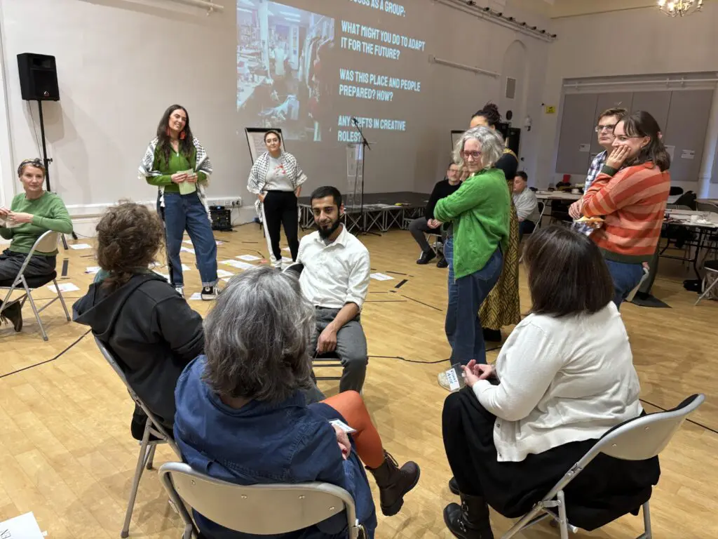 Inside a large meeting room with a projected slide on the wall, a seminar participants gather in the foreground