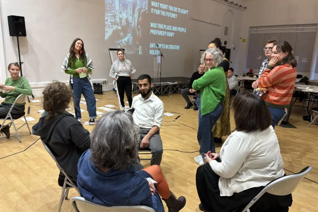 Inside a large meeting room with a projected slide on the wall, a seminar participants gather in the foreground