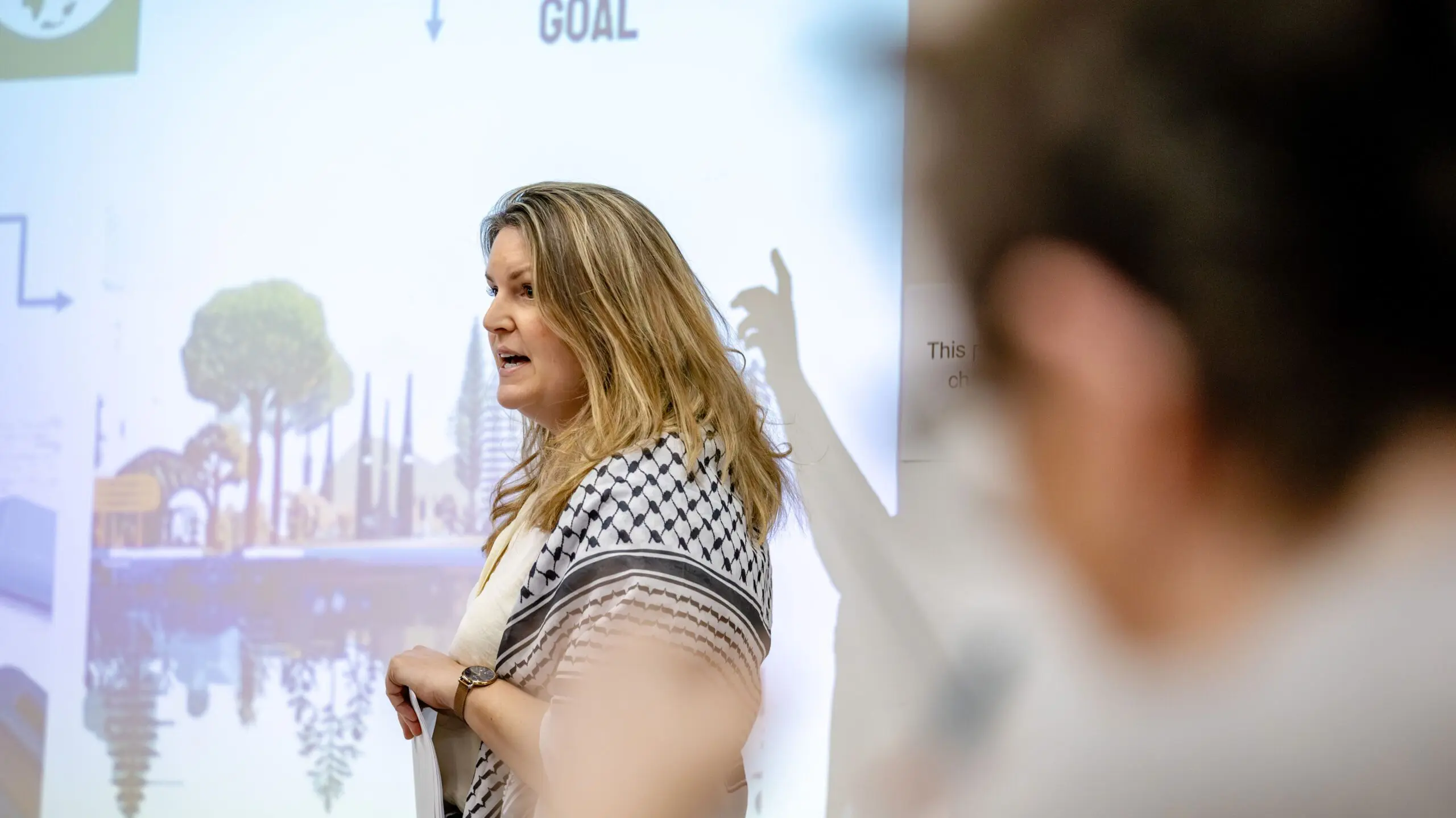 Woman with blond hair wearing a keffiyeh giving a presentation