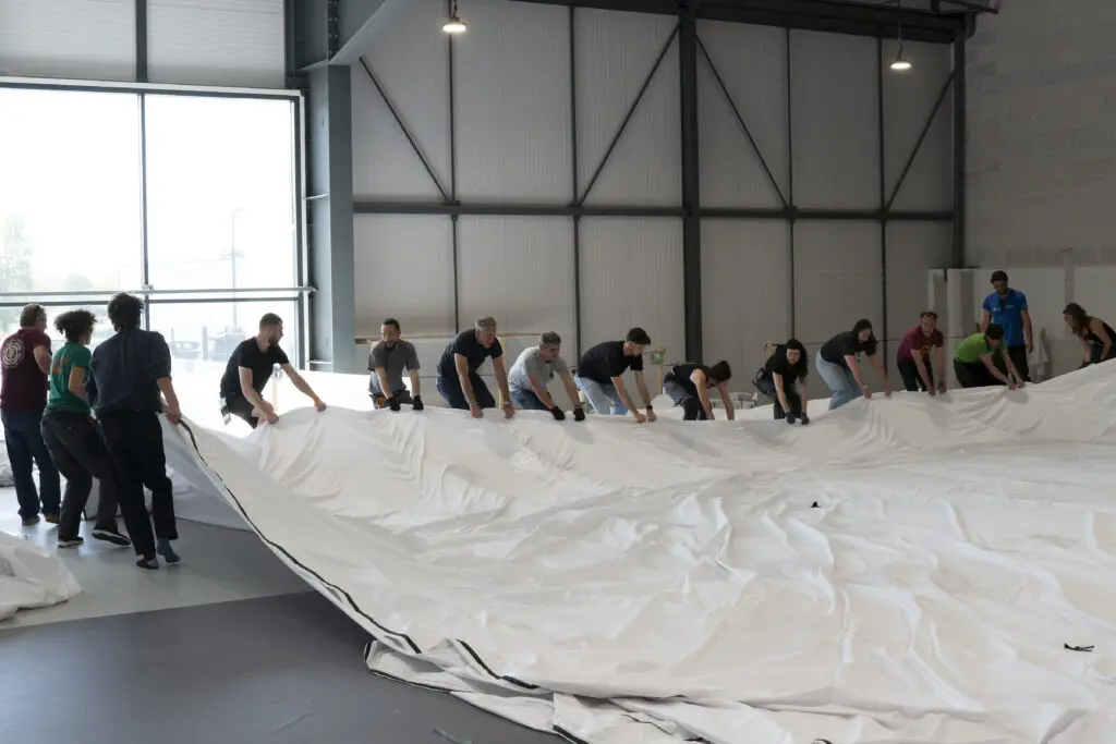 A team of people haul white fabric through a warehouse