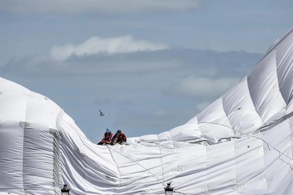 Two people sitting on the white parachute-like fabric of Pont Neuf as it is constructed